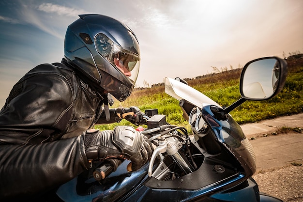 Motociclista con casco e giacca di pelle che gareggia sulla strada