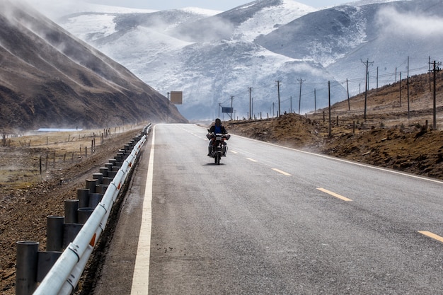 Motociclista del motociclista durante il bello inverno della strada in Tibet sotto la montagna della neve, Sichuan, Cina