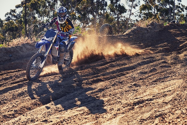 Motociclista e velocità con nuvola di polvere per giochi concorso o sfida in ritratto per sport estremi Persona motocicletta e sporcizia su sentiero strada e sentiero in natura per trasporto veloce in estate