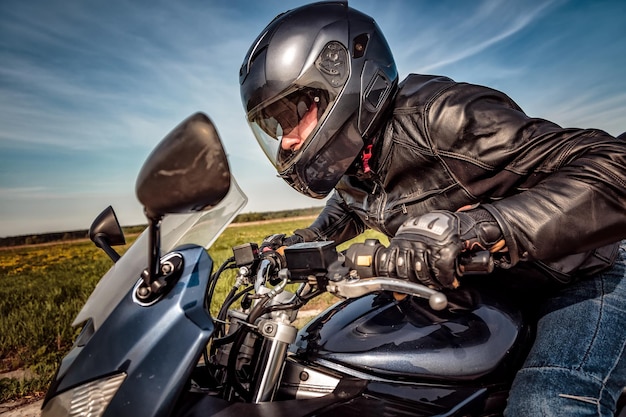 Motociclista in casco e giacca di pelle che corre su strada