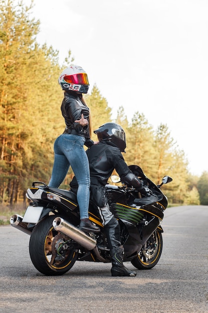 Motociclista in equipaggiamento protettivo e casco mostra scopare con un dito medio mentre è seduto con una ragazza su una moto