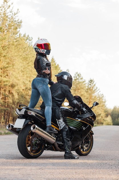 Motociclista in equipaggiamento protettivo e casco mostra scopare con un dito medio mentre è seduto con una ragazza su una moto