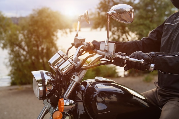 Motociclista in sella a una moto vicino al fiume in città. Primo piano del manubrio