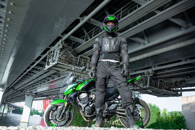 Motociclista in un casco e in una tuta protettiva si trova sotto il ponte