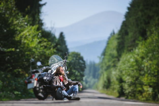 Motociclista maschio che si siede sulla strada vicino al motociclo