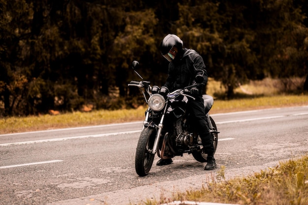 motociclista maschio in uniforme protettiva e casco con motociclista personalizzato cafè racer in autunno su Th