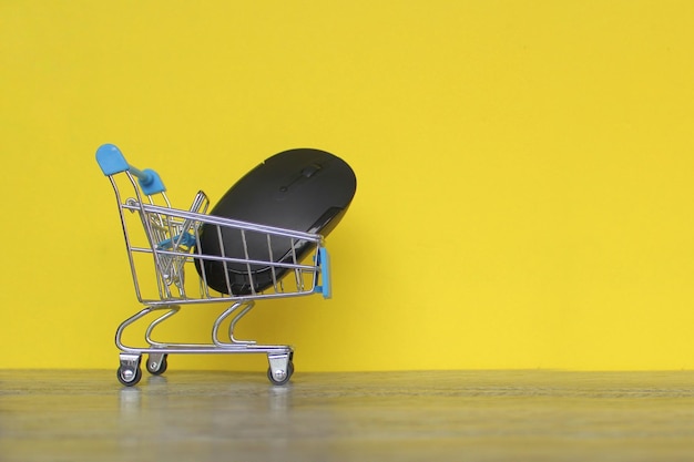 Mouse del computer all'interno del carrello della spesa su sfondo giallo con spazio per la copia Concetto di shopping online