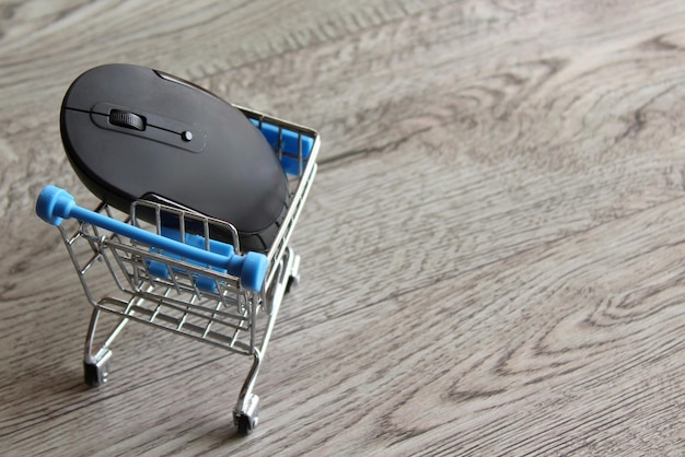 Mouse del computer all'interno del carrello della spesa su tavolo di legno con spazio per la copia Concetto di shopping online
