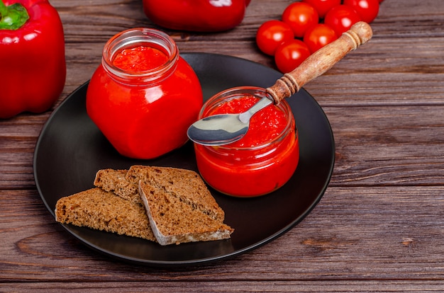Mousse al pepe di paprika e pomodori in barattoli di vetro in un piatto nero su un tavolo di legno rustico