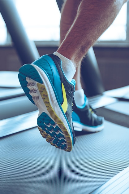 Movimento e forza. Parte ravvicinata dell'uomo in scarpe sportive che corre sul tapis roulant in palestra