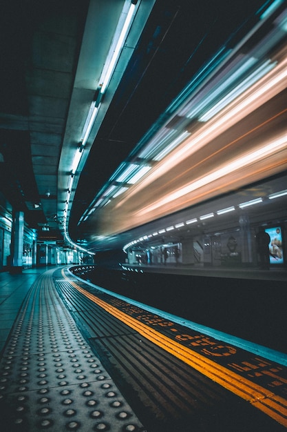 Movimento sfocato del treno sulla piattaforma della stazione ferroviaria durante la notte