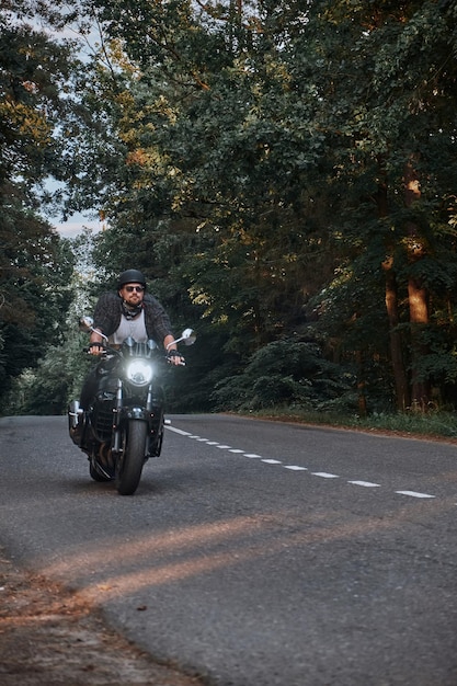 Movimento sfocato un giovane motociclista in un casco cavalca rapidamente ad alta velocità su una strada forestale in movimento