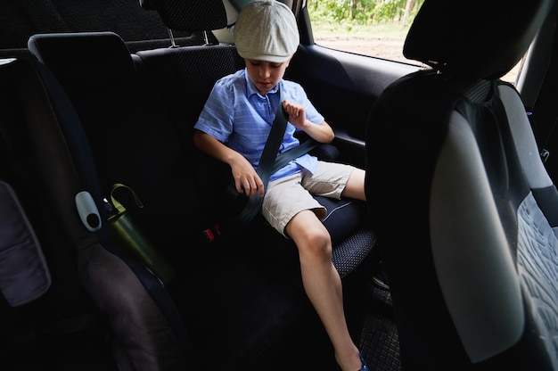 Movimento sicuro dei bambini in macchina. Un ragazzo adorabile allaccia la cintura di sicurezza del suo seggiolino all'interno dell'auto. Concetti di trasporto per la sicurezza dei bambini