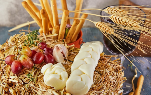 Mozzarella a forma di treccia con uva nel fieno con orecchie di pane su sfondo blu