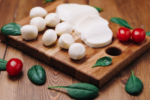 Mozzarella bianca piccola, palline di formaggio, foglie di spinaci e pomodori su tavola di legno