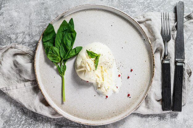 Mozzarella Burrata su un piatto bianco con foglie di basilico. Sfondo grigio. Vista dall'alto