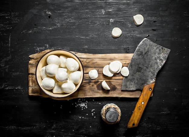 Mozzarella fresca con un'accetta per il taglio su un fondo di legno nero