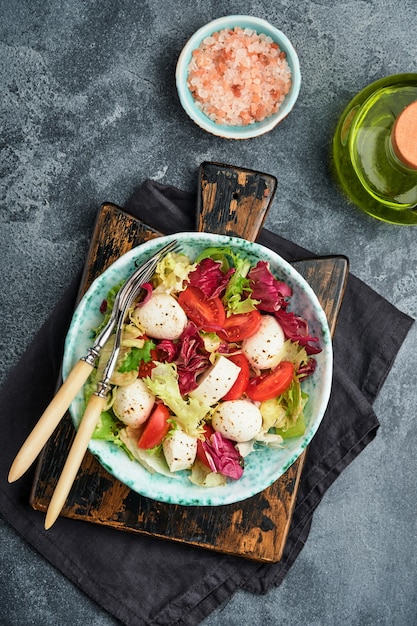 Mozzarella, pomodoro e misticanza di foglie di insalata fresca, fondo scuro