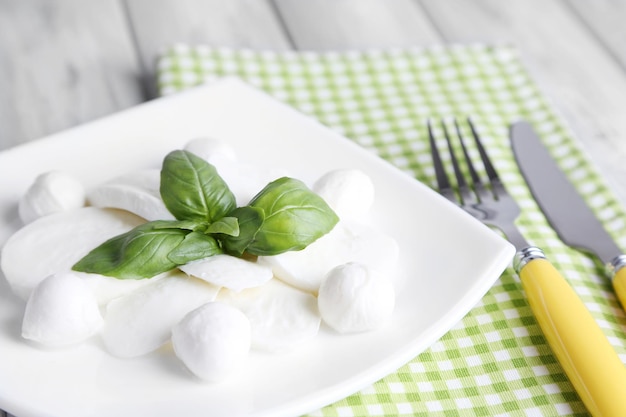 Mozzarella saporita con basilico sul piatto su fondo di legno