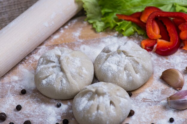 Mucchio del primo piano crudo casalingo degli gnocchi di khinkali con le verdure sul bordo