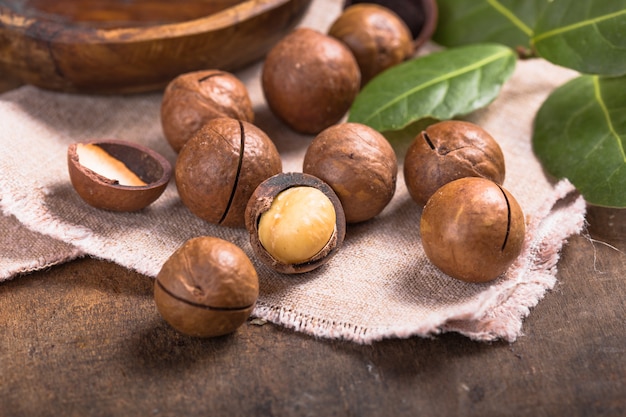 mucchio delle noci di macadamia con le coperture in borsa sulla tavola di legno