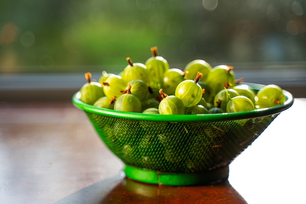 Mucchio di frutta verde uva spina lavata bagnata in uno scolapasta sul tavolo.