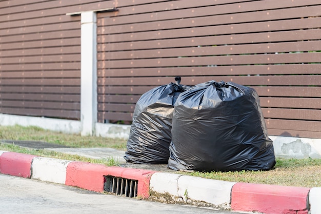 Mucchio di immondizia nera sul sentiero per pedoni al cestino dell'inquinamento della strada laterale