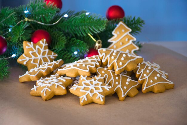 Mucchio di pan di zenzero tradizionale a forma di albero di Natale e fiocco di neve vicino a rami di abete rosso giocattoli e luci