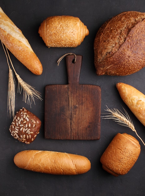 Mucchio di pane operato intorno al tagliere di legno su fondo di pietra nero