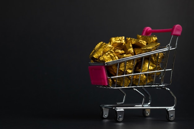 mucchio di pepite d&#39;oro o minerale d&#39;oro nel carrello del carrello o del supermercato su sfondo nero