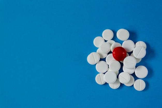 Mucchio di pillole bianche e una rossa su sfondo blu