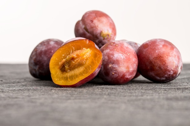 Mucchio di prugne fresche intere con una metà bilanciata davanti che mostra la consistenza succosa della polpa arancione e del nocciolo o del seme, angolo basso con copyspace.