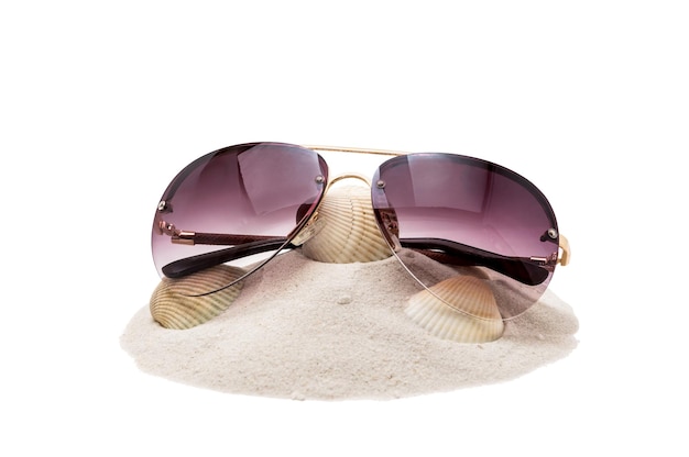 Mucchio di sabbia con conchiglia e occhiali da sole isolati su bianco
