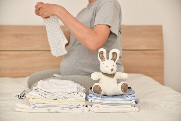 Mucchio di vestiti per bambini con un coniglio e una donna incinta