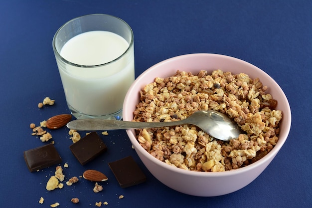 muesli al cioccolato e banana in una ciotola rosa con cucchiaio e bicchiere di latte, primo piano