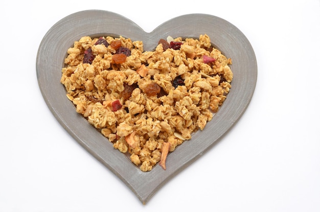 Muesli biologico tradizionale con frutta secca in una cornice a forma di cuore su sfondo bianco