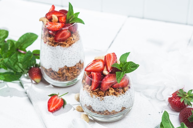 Muesli con yogurt chia e fragole in un bicchiere su sfondo bianco