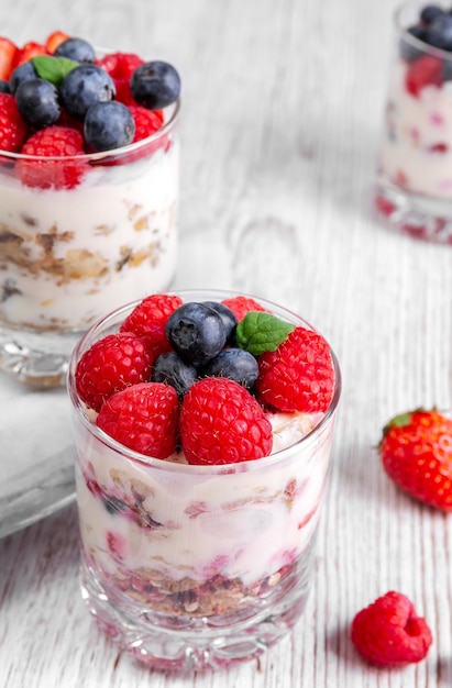 Muesli con yogurt e frutti di bosco in un bicchiere su sfondo bianco