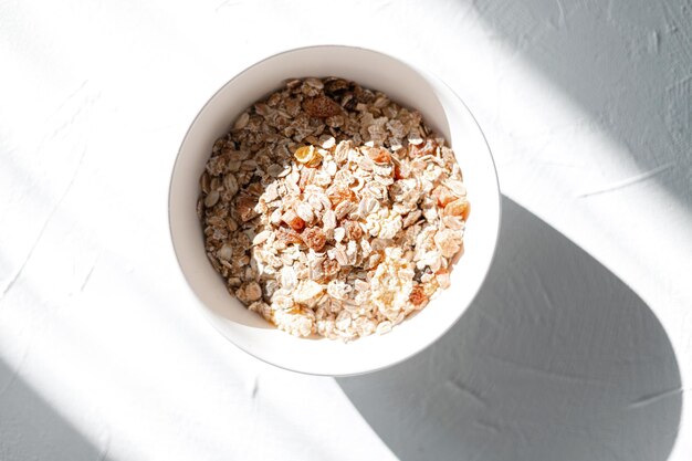 Muesli di cibo sano con farina d'avena e frutta secca in una ciotola bianca su un piatto bianco al sole, vista dall'alto