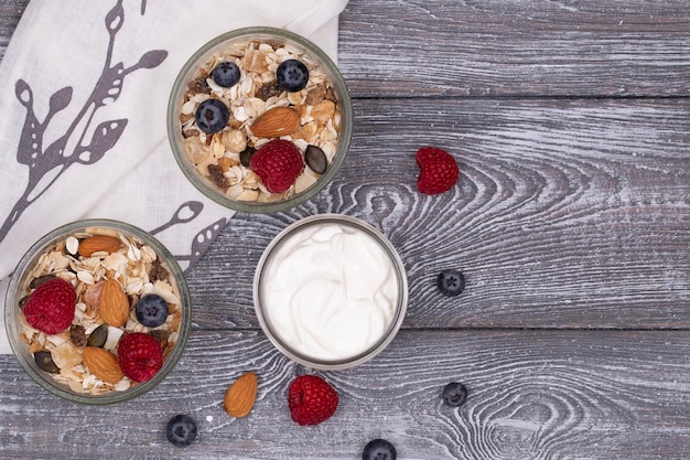 Muesli fatti in casa con lamponi noci e yogurt ai mirtilli su un tavolo rustico imbiancato grigio