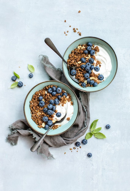 Muesli fatti in casa con mirtilli maturi serviti in due ciotole con yogurt greco fresco, vista dall'alto in basso