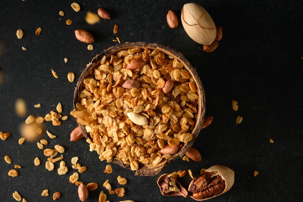 Muesli fatti in casa con noci in una ciotola di cocco e muesli che cadono dall'alto su una superficie grigio scuro