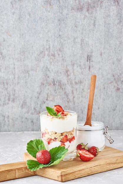 Muesli o yogurt con fragole in vetro, bacche fresche e vaso con zucchero sul tagliere