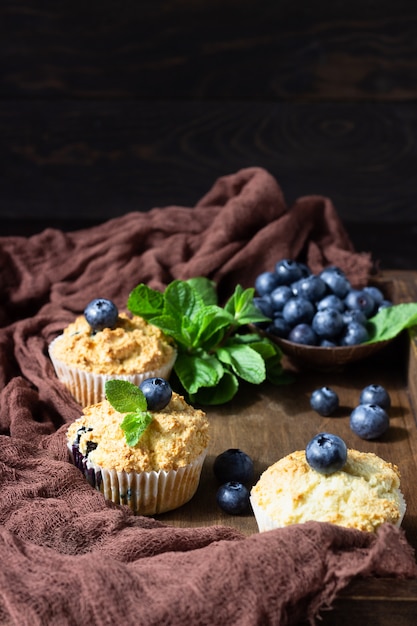 Muffin ai mirtilli con le bacche e la menta fresche in un vassoio di legno.
