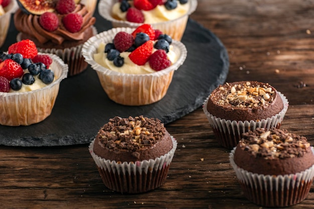 Muffin al cioccolato con noci e muffin alla vaniglia con mix di frutti di bosco freschi su tavola di legno