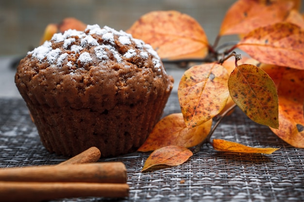 Muffin al cioccolato con ripieno di mele su uno sfondo di foglie di autunno e cannella