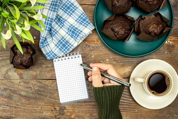 muffin al cioccolato fatti in casa o madeleine in piatto verde con una tazza di caffè e un vaso di fiori di giglio