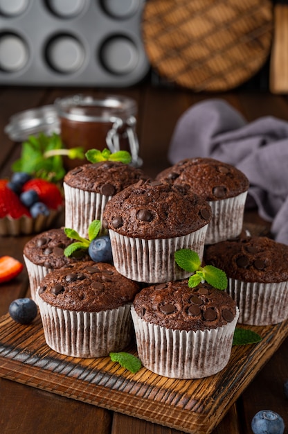 Muffin al cioccolato o cupcakes con gocce di cioccolato su una tavola di legno con frutti di bosco freschi e menta