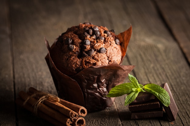 Muffin al cioccolato scuro cotto con menta su un tavolo di legno con cannella, anice, cioccolato.