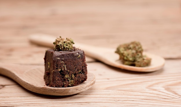 Muffin al cioccolato su cucchiaio di legno con germogli di cannabis Torta alla marijuana su un tavolo di legno marrone